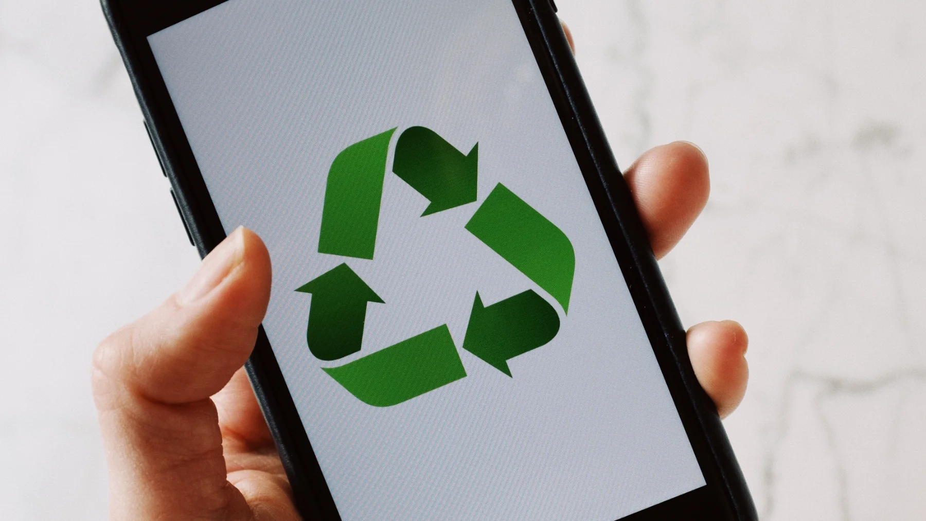 A hand holding a smartphone displaying a green recycling symbol on the screen, representing the concept of a digital circular economy.