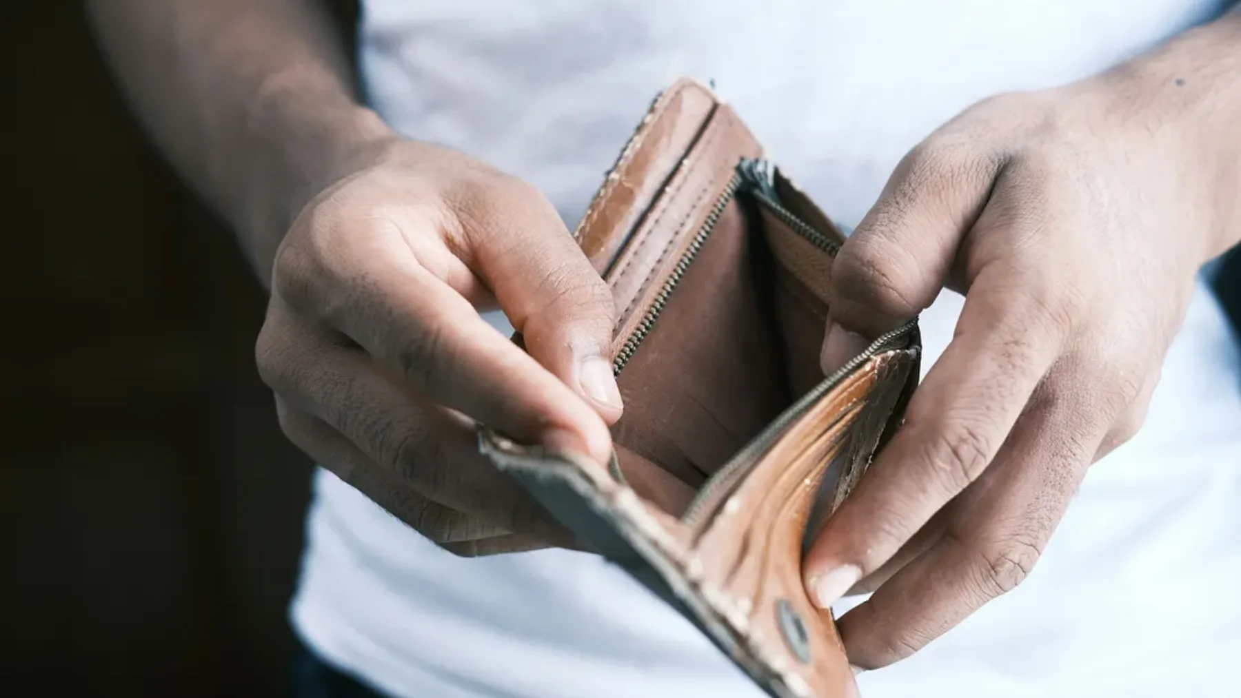 A farmer holding open an empty brown leather wallet